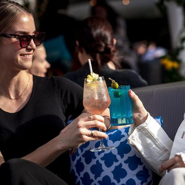 Two women drinking cocktails on a sunny rooftop bar